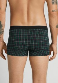 Svarta kalsonger med grönt och blått rutmönster. Svart elastisk midjeband. Tyget verkar slätt med en tight passform.