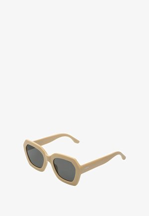 Lunettes de soleil oversize beiges avec des montures hexagonales et des verres foncés. Texture lisse avec des branches élégantes. Marquage minimal sur une branche.