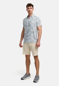 Kortærmet, lyseblå skjorte med hvid palmeblad mønster og mørke knapper, parret med beige shorts og grå sneakers.