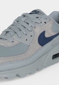 Светлосив и син Nike маратонка с мрежести и велурени панели, синьо лого swoosh, сиви връзки и видима подметка Air Max.