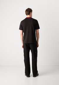 Black short-sleeve t-shirt with red accent at the collar, paired with black cargo pants featuring side pockets and a relaxed fit.