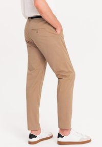 Pantaloni beige con vestibilità slim, dotati di tasche posteriori e cintura. Abbinati a sneakers bianche con dettagli neri sul tallone.