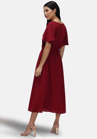 Burgundy midi-mekko, jossa on lyhyet leijuvat hihat, kireä vyötärö ja hilpeä hame. Yhdistetty vaaleanbeigeihin nauhoihin.