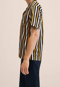 Camisa de manga corta con rayas verticales en amarillo, azul marino y blanco, de corte holgado y con cuello, confeccionada en tela ligera.