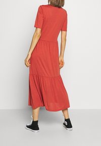 Rotes Jerseykleid mit kurzen Ärmeln, gerafftem Bund und schichtender Rock. Kombiniert mit schwarzen High-Top-Sneakers. Glatte Textur und lässiges Design.