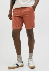 Rust-colored shorts made of cotton, featuring rolled cuffs, spacious side pockets, and paired with white and blue sneakers.