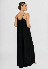 Schwarzes Maxikleid mit einer lockeren, fließenden Silhouette, schmalen Trägern und gerafftem Rückendetail. Hergestellt aus weich, leichtem Stoff.