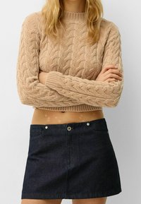 Béžový svetr s dlouhými rukávy a patentovaným lemem, spojený s tmavě modrou džínovou minisukní s předními kapsami a zapínáním na knoflíky.
