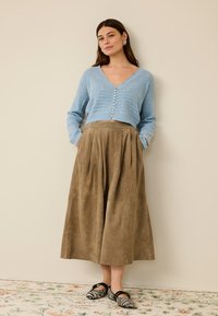 Svijetloplavi pleteni kardigan s gumbima sprijeda, upareno s smeđom ante plisiranom midi suknjom i crno-bijelim prugastim cipelama.