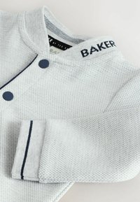 Hellgraue gestreifte Jacke mit rundem Kragen, auf dem "BAKER" in Marineblau gestickt ist, mit Knopfverschluss und Marineblauem Besatz an den Ärmeln.