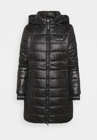 Giacca lunga trapuntata nera con cappuccio, chiusura frontale con zip, tasche laterali con zip e logo Calvin Klein sul petto e sui polsini.