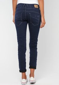 Marineblå jeans med slim fit, som har bakfickor, en texturerad yta och uppvikta ärmar. Inkluderar en beige logopatch på midjebandet.