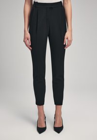 Zwarte op maat gemaakte broeken met een hoge tailleband, met plooien, een slim fit en een verkorte lengte. Draagt zwarte spitse hakken.