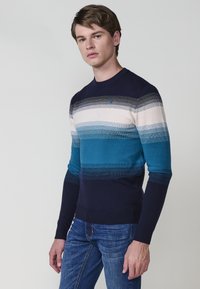 Jersey de punto con rayas horizontales en azul, verde azulado y crema. Cuello redondo, mangas largas, puños acanalados y dobladillo. Tela ligera.