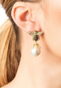 Pendiente en forma de abeja dorada con adornos en blanco y negro, que presenta un gran colgante de perla blanca lustrosa debajo.