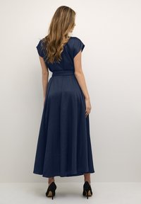 Navy blue maxi dress with short sleeves, fitted waist, and flowy skirt, made of smooth fabric. Worn with black stiletto heels.