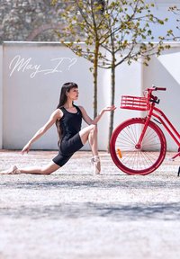 Een rode fiets met een mand staat naast een figuur in een zwart sportoutfit, die een danspose uitvoert op een grindachtige ondergrond.