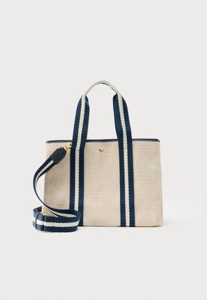 Sac fourre-tout en tissu beige avec des poignées rayées bleu marine et blanc et une bandoulière amovible, doté d'une petite fermeture à bouton doré.