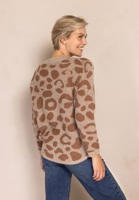 Beiger Pullover mit braunem Tiermuster, langen Ärmeln und rundem Ausschnitt, kombiniert mit blauen Jeans.