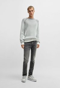 Maglione a coste grigio chiaro con collo rotondo, abbinato a jeans slim-fit grigio scuro e sneakers grigio chiaro. Outfit semplice e casual.