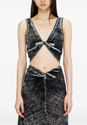 Donna che indossa un top corto senza maniche nero e argento con trama e gonna abbinata con dettagli di nodi intrecciati sul davanti.