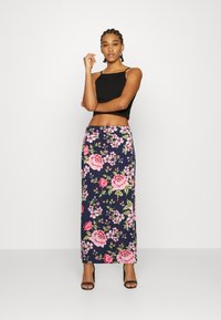 Top cropped preto e saia maxi floral azul-marinho com grandes rosas cor-de-rosa e brancas, folhas verdes e um design ajustado. Sandálias de salto pretas.
