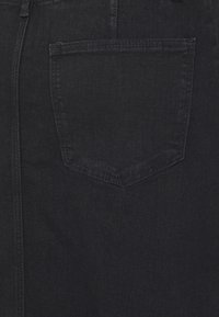 Tissu en denim noir avec une poche arrière unique en forme de losange, des coutures renforcées et une texture lisse.