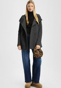 Grijze, gestructureerde jas met een brede kraag en dubbele knopen, gecombineerd met donkere jeans en een tas met luipaardprint. Bruine enkellaarsjes.