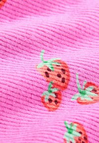 Tessuto rosa a coste con piccole fragole stampate in rosso e verde. La texture è morbida, con un motivo di frutta giocoso in tutto il tessuto.