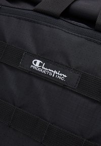 Surface en tissu noir avec des sangles noires cousues et une étiquette rectangulaire noire portant l'inscription "Champion PRODUCTS INC." en texte blanc.