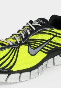 Αθλητικό παπούτσι Nike σε νέον κίτρινο και μαύρο με λευκά κορδόνια και διαιρεμένη λευκή σόλα για ευκαμψία και υποστήριξη.