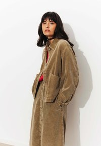 Ensemble en velours côtelé beige composé d'une veste et d'une jupe avec un motif à côtes texturé. La veste présente un col, des boutons et deux poches avant.