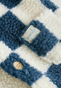 Blaue und weiße karierte Fleece-Stoff mit einer strukturierten Oberfläche, einem angenähten Etikett mit der Aufschrift "Lächle, kleines Kind" und einem Holzknopf-Detail.