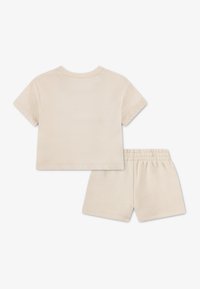 Σετ δύο τεμαχίων από μπεζ βαμβάκι με τοπ κοντομάνικο και στρογγυλή λαιμόκοψη και ταίριαστο σορτς με ελαστική μέση.