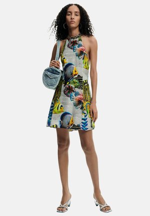 Naine kannab varrukateta kaelusega kleiti, millel on värvikad troopilised kalad ja korallimustrid, hoides õlal väikest teksakotti.