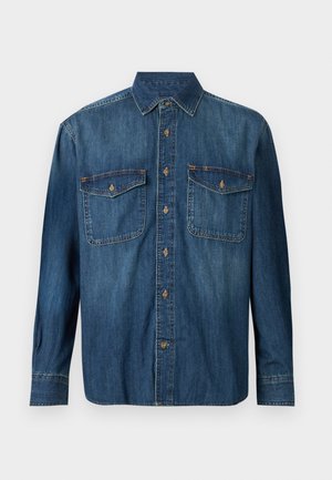 Camisa de mezclilla de manga larga con botones, con dos bolsillos en el pecho y puños abotonados en un lavado azul medio.