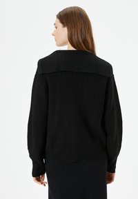 Schwarzer gestrickter Pullover mit weitem Kragen, gerippter Textur und langen Ärmeln. Einfaches Design in lässiger Passform mit überschnittenen Schultern.