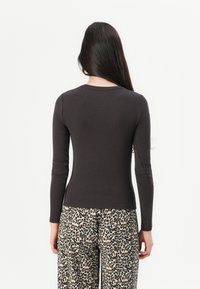 Langärmliges, dunkelgraues Oberteil mit Rundhalsausschnitt, figurbetonter Silhouette und glatter Textur, kombiniert mit weitem Leopardenmuster-Hosen.