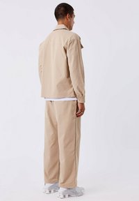 Beige katoenen shirt en bijpassende broek, relaxed fit, achteraanzicht. Het shirt heeft een kraag en knopen; de broek is wijduitlopend met zijzakken.