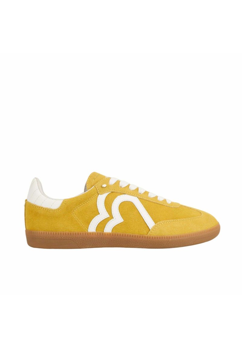 Baskets en daim jaune avec des accents en cuir blanc, présentant un design de logo unique sur le côté, une semelle en gomme caoutchouc et un système de laçage.
