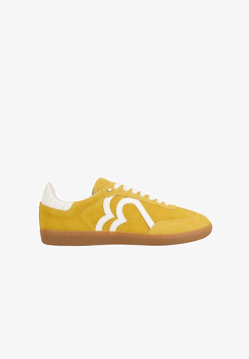 Baskets en daim jaune avec des accents en cuir blanc, présentant un design de logo unique sur le côté, une semelle en gomme caoutchouc et un système de laçage.