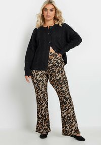 Cardigan in maglia nera a treccia con maniche lunghe e bottoni, abbinato a pantaloni a vita alta svasati in stampa animale nei toni del marrone e del nero.