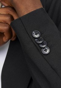 Zwarte colbertmanchet met een gestructureerde stof, drie donkere knopen met elk vier gaten, en zichtbaar stiksel. 