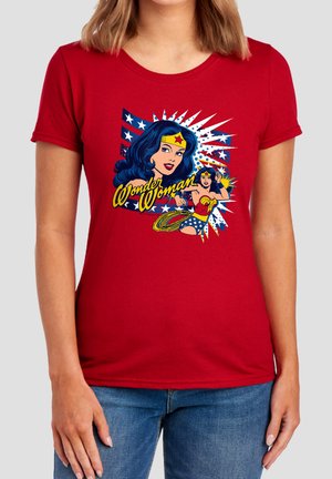 Frau trägt ein rotes T-Shirt mit buntem Wonder Woman-Design und Text, kombiniert mit blauen Jeans.