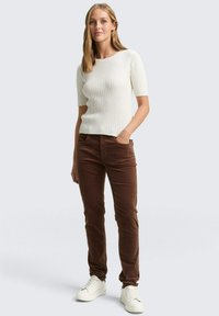 Witte geribbelde short-sleeve trui met een V-vormig patroon aan de voorkant, gecombineerd met bruine corduroy broeken en witte sneakers.