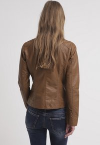 Brun läderjacka med en figursydd design, synliga sömdetaljer och en midjelång passform, kombinerad med mörka denimjeans.