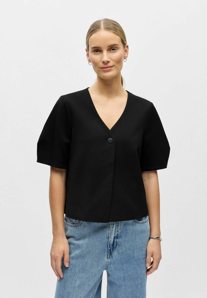 Blouse noire courte avec manches courtes bouffantes et col en V profond. Dispose d'une fermeture à bouton unique à l'avant. Texture de tissu lisse.