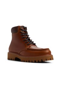 Botín de cuero marrón hasta el tobillo con punta redonda, cordones grises y suela de goma resistente. Presenta un estilo de mocasín cosido y soporte acolchado para el tobillo.