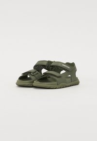 Green sandals with adjustable Velcro straps, textured sole, and cut-out design elements. Lightweight material designed for breathability.