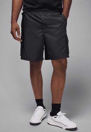Schwarze Cargo-Shorts mit elastischem Bund, zwei Seitentaschen und einer Cargo-Tasche. Hergestellt aus leichtem Stoff mit glatter Textur.